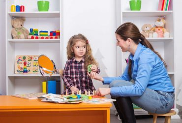 Toddler girl in child occupational therapy session doing sensory playful exercises with her therapist.
